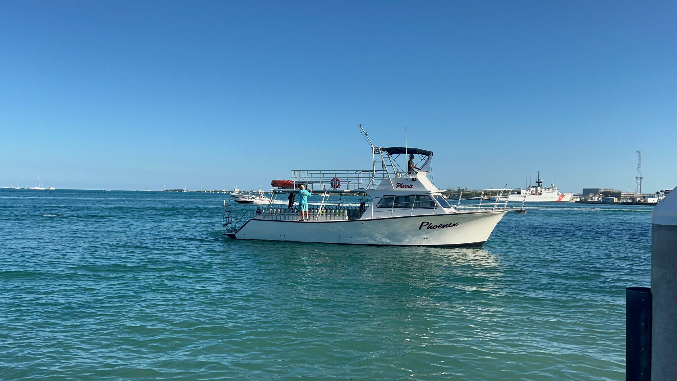 White boat named 'Phoenix' on blue ocean near harbor.