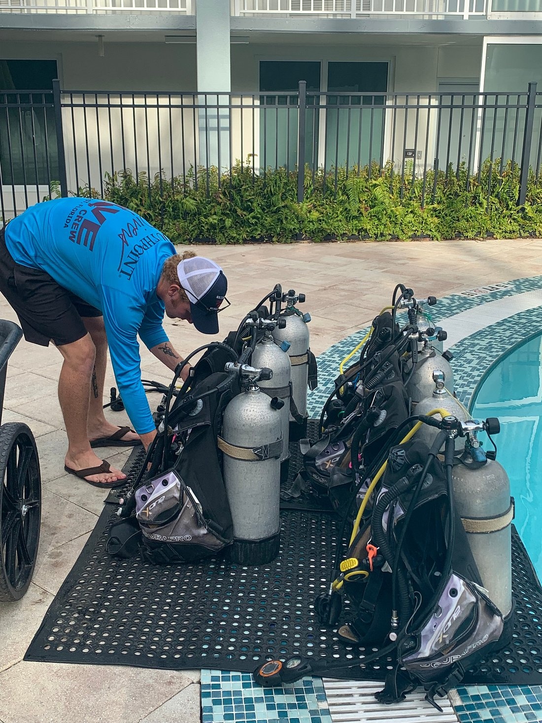 Person in blue shirt setting up scuba gear by a pool.