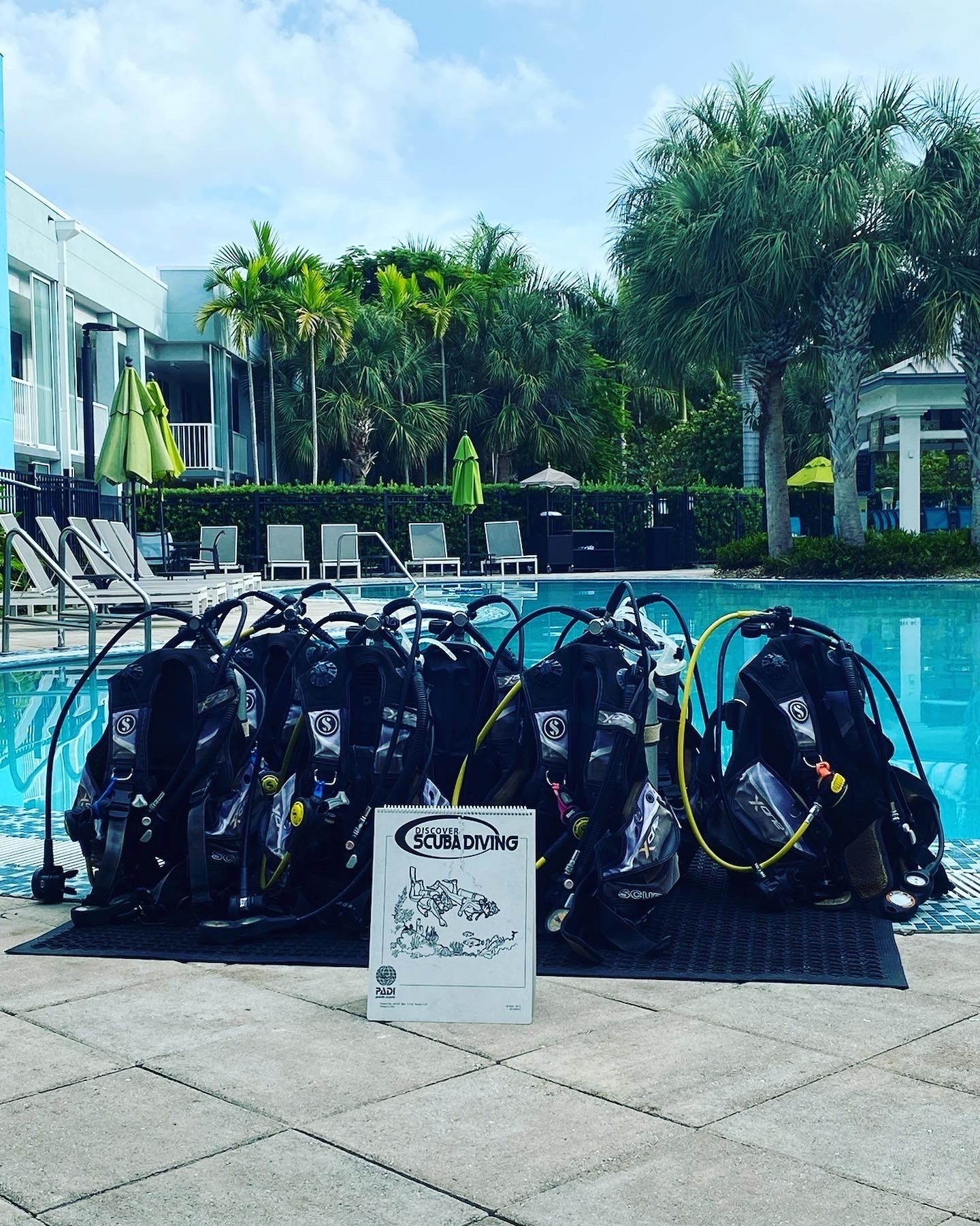 Scuba gear set beside a swimming pool with palm trees in the background.
