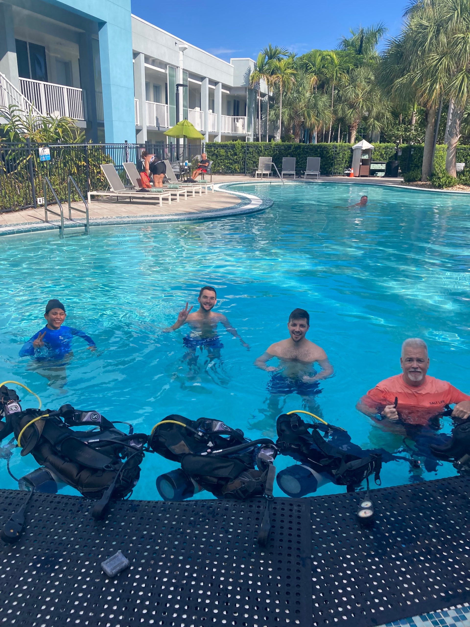 Group of people in a pool, with diving gear nearby on a sunny day.