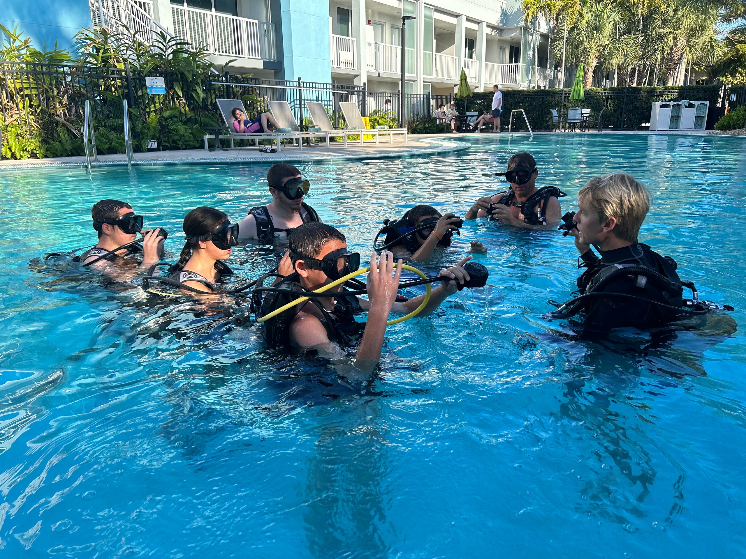 People in scuba gear receiving instructions in a swimming pool.