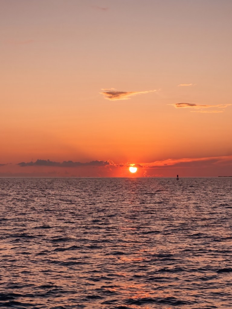 Sunset over calm ocean with orange sky and clouds.