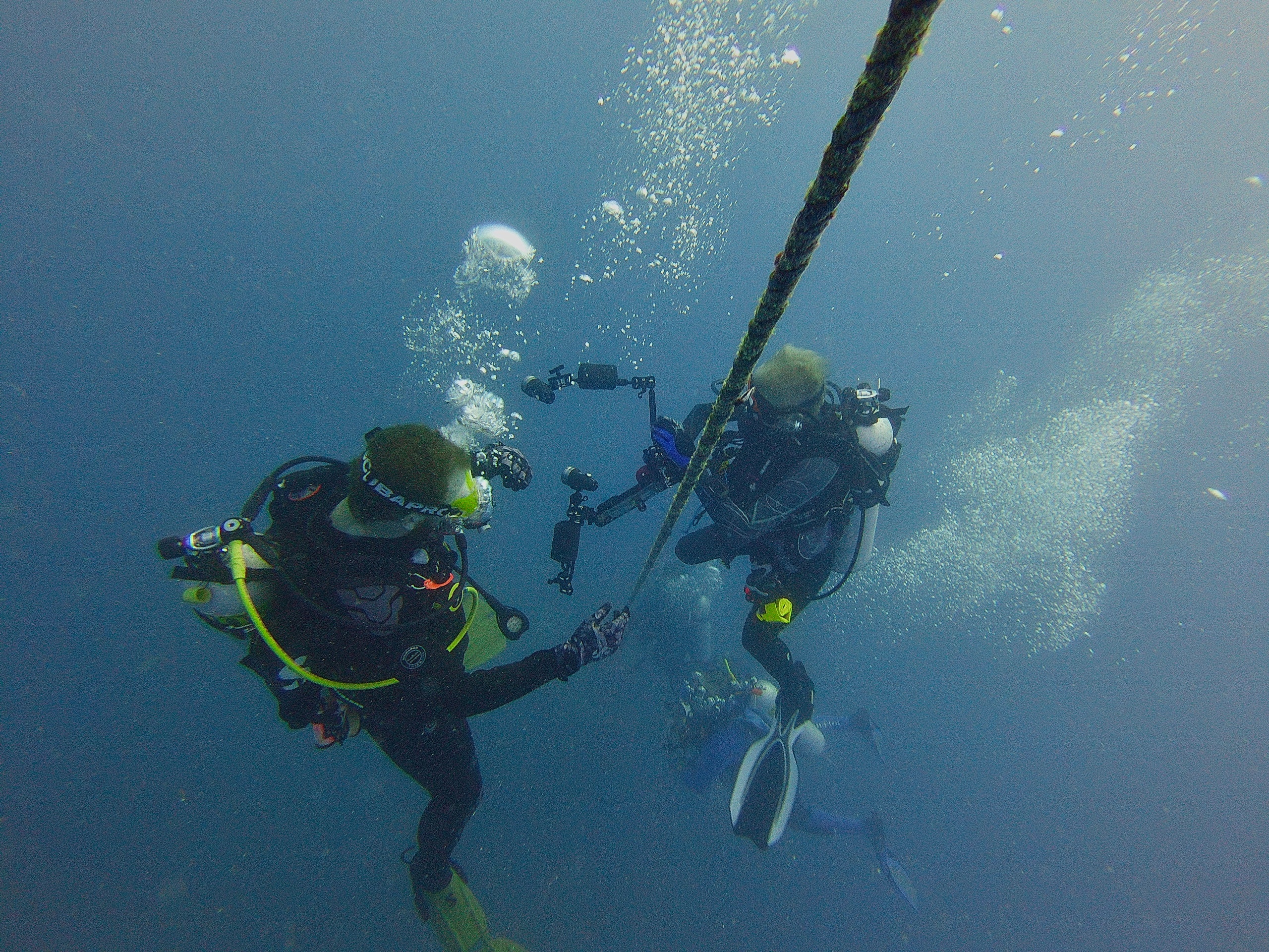 Three divers underwater holding onto a rope with equipment.