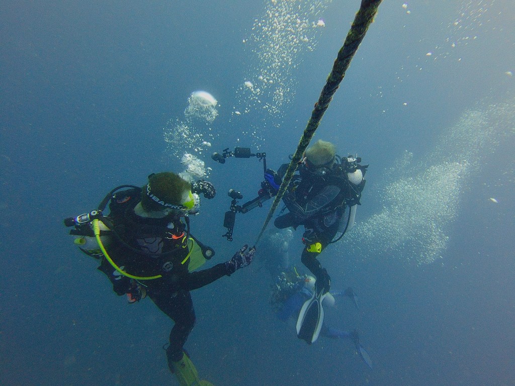 Three divers underwater holding onto a rope with equipment.