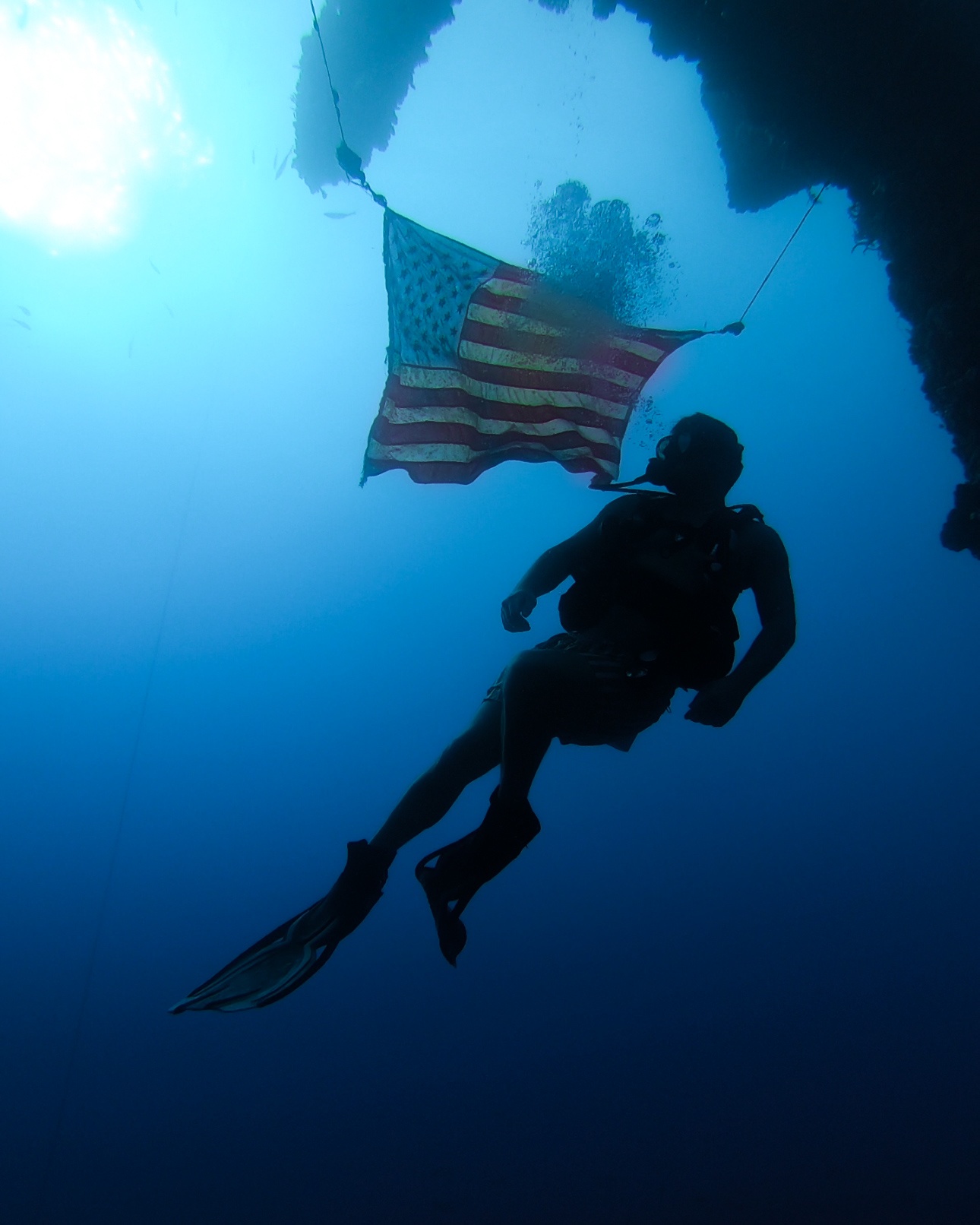Diver under water with an American flag in a cave.