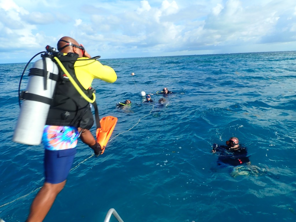 Divers in ocean; one on boat in gear, others in water, cloudy sky.