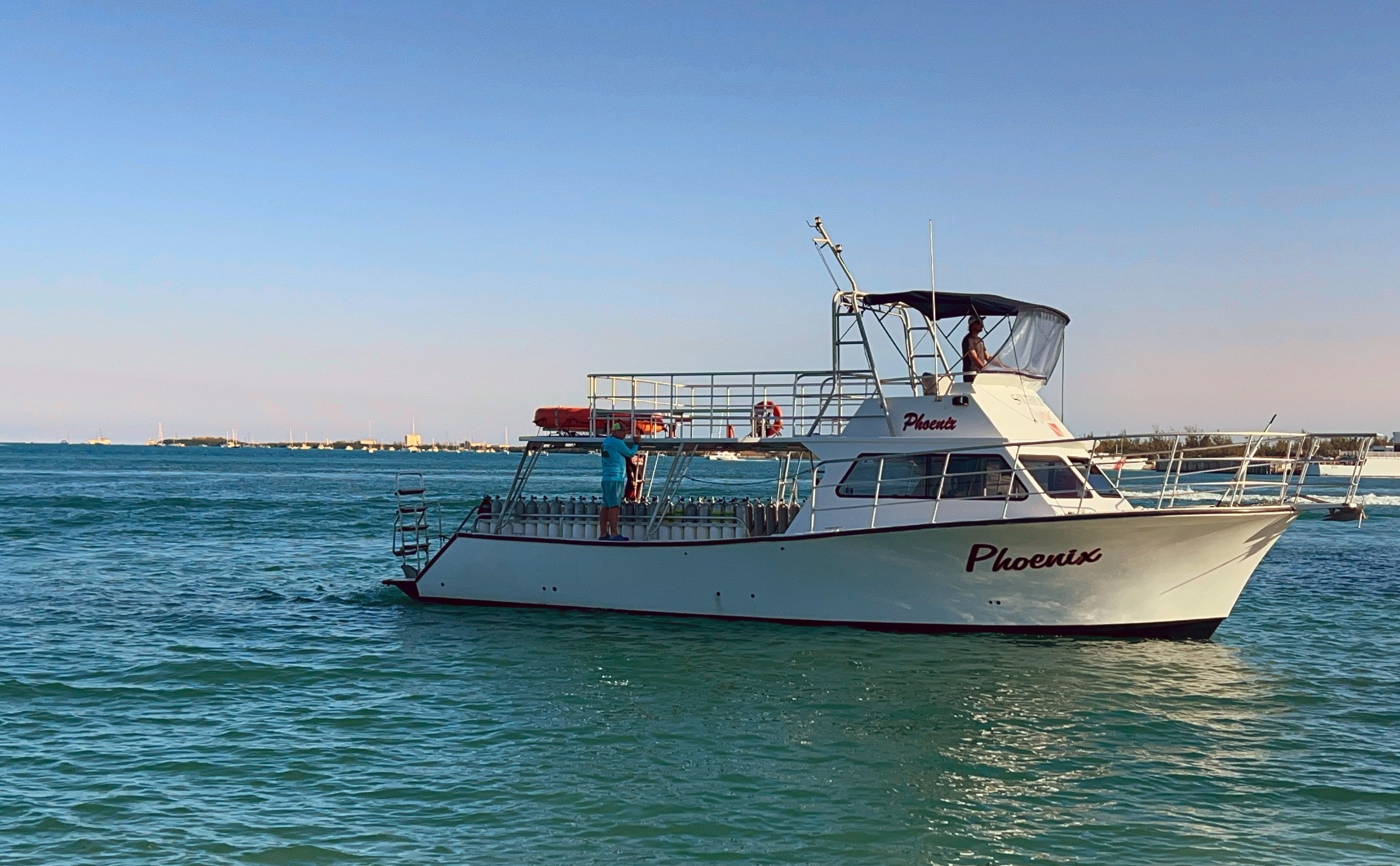 White boat named Phoenix on calm blue water against clear sky.