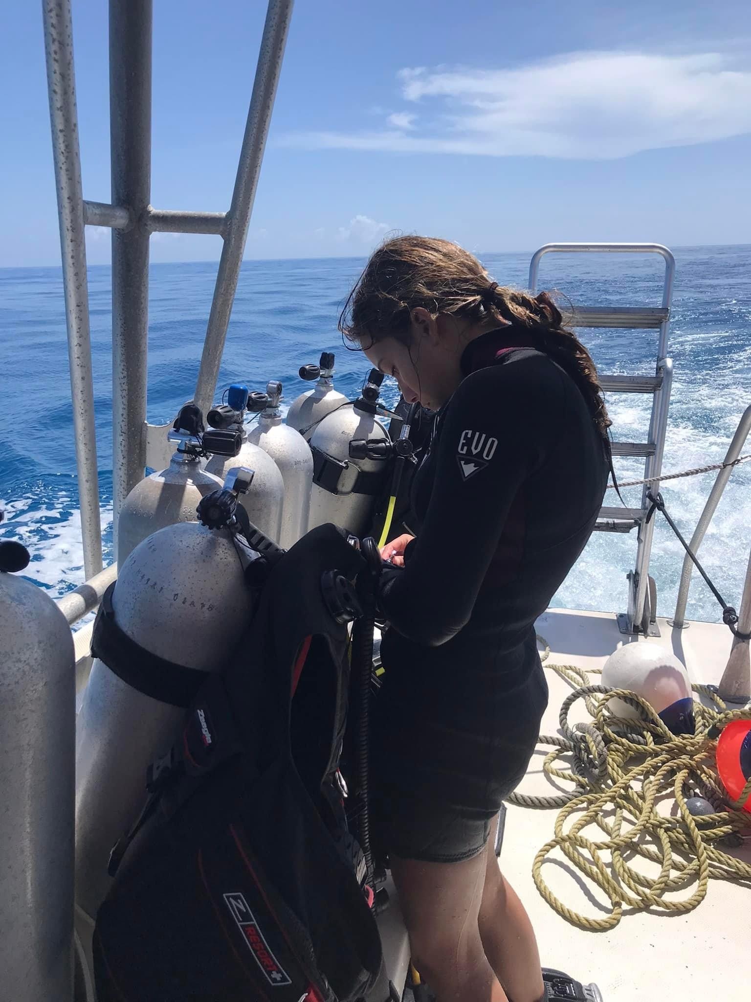 Person in wetsuit preparing scuba gear on a boat.