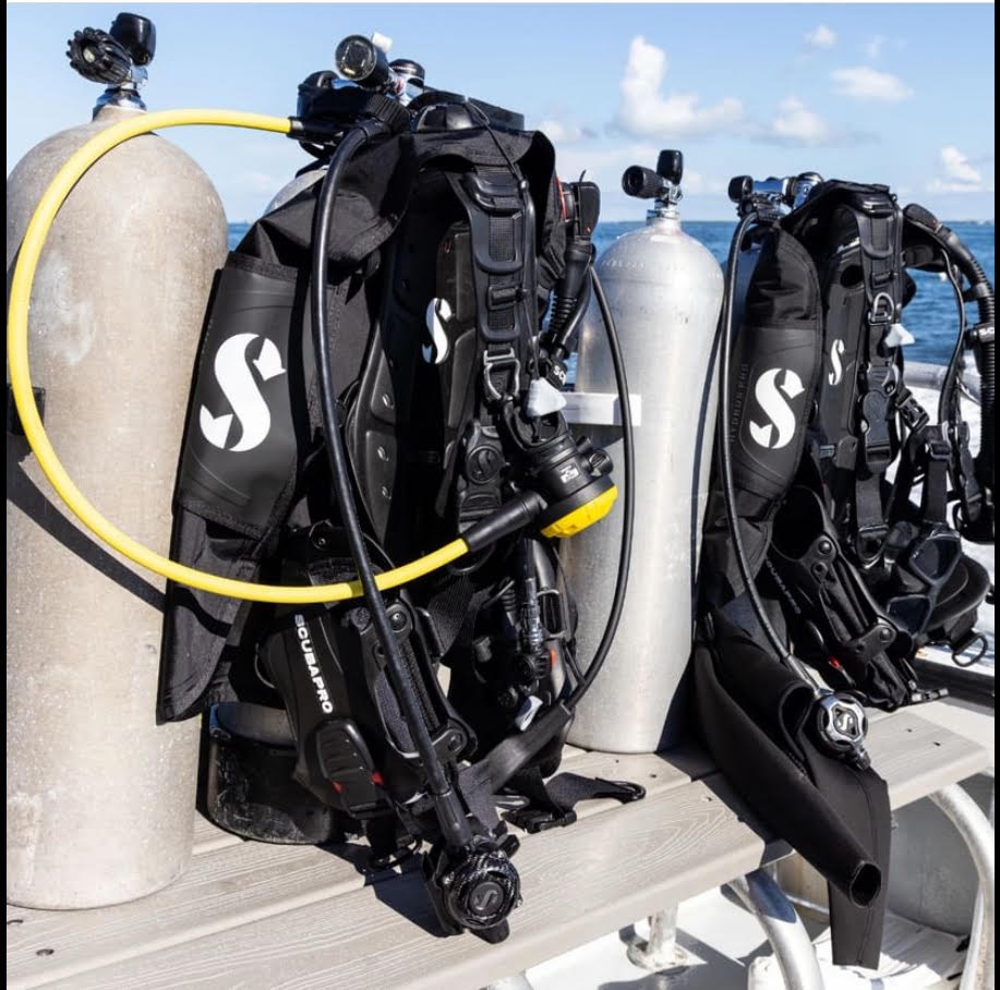 Two sets of scuba gear with tanks on a boat, ocean background.