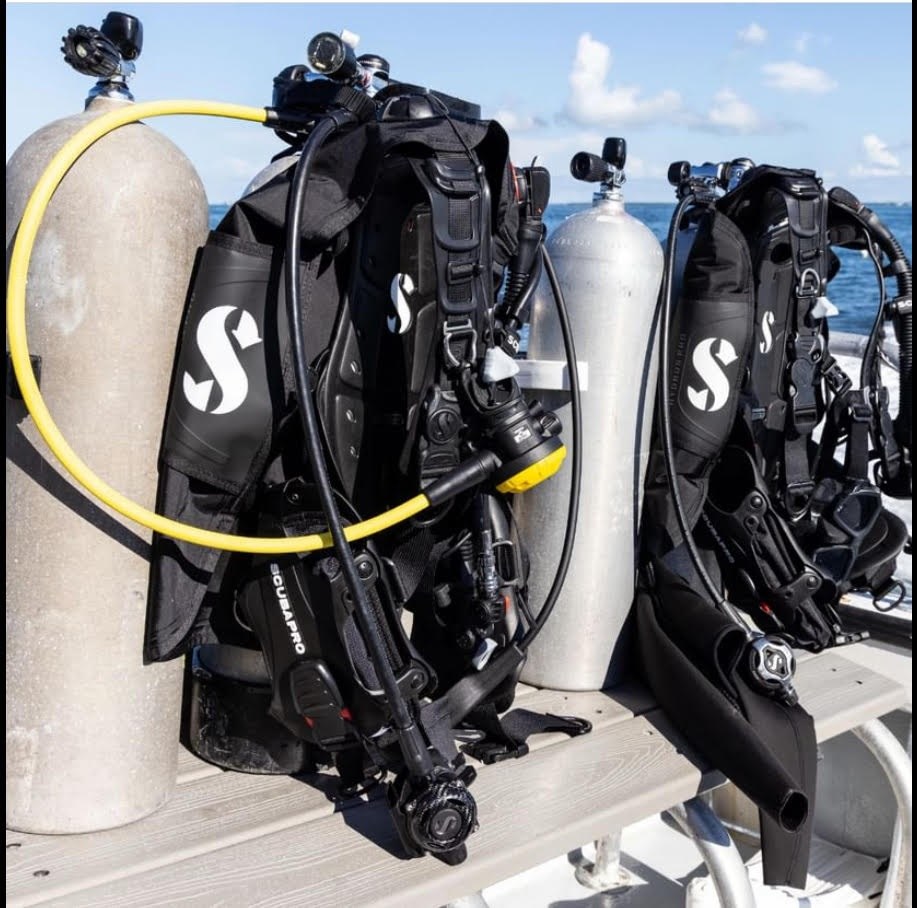 Two sets of scuba gear with tanks on a boat, ocean background.