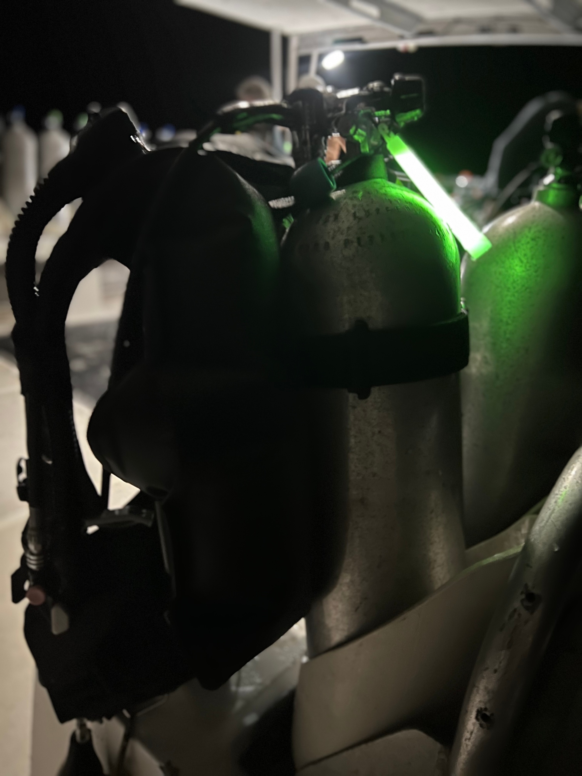 Scuba tanks on a boat deck, dimly lit with a green light.
