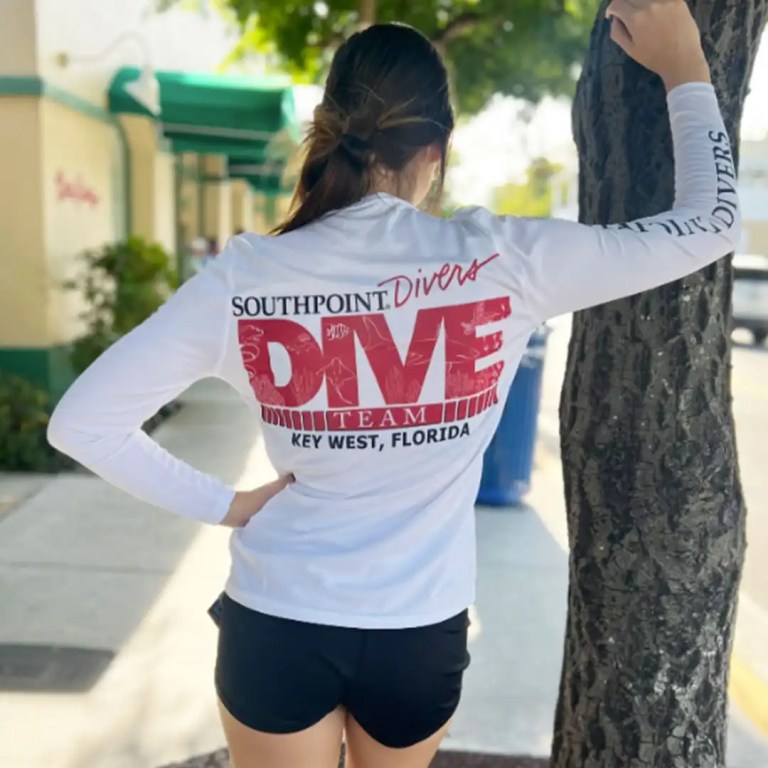Person wearing a white Southpoint Divers shirt stands by a tree.