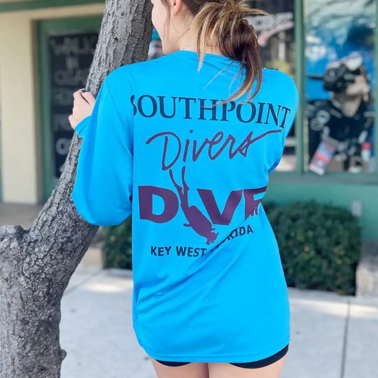 Person in blue 'Southpoint Divers' shirt leans on tree.
