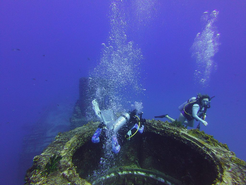 Two scuba divers exploring a submerged structure underwater.