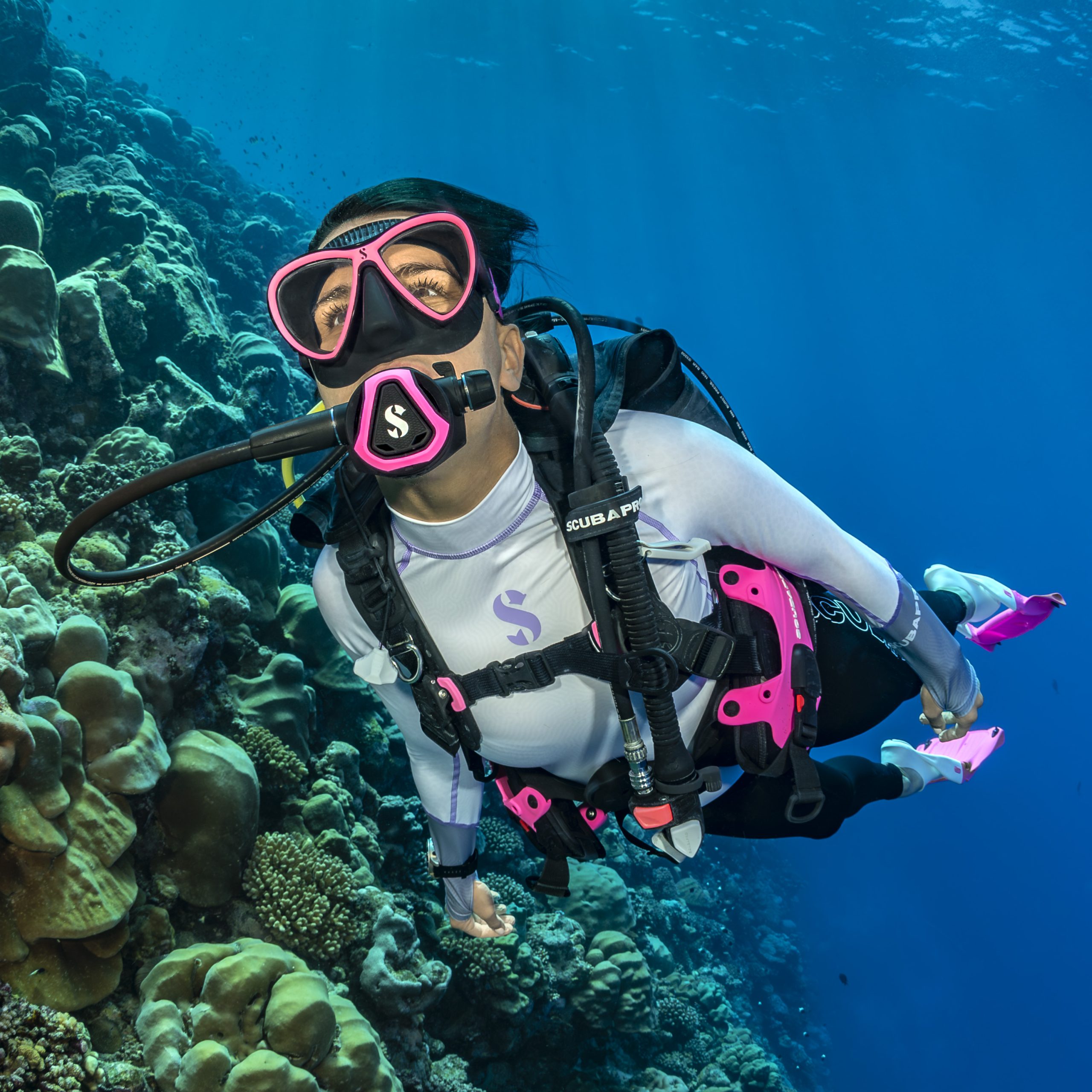Person scuba diving near coral reef in blue ocean.