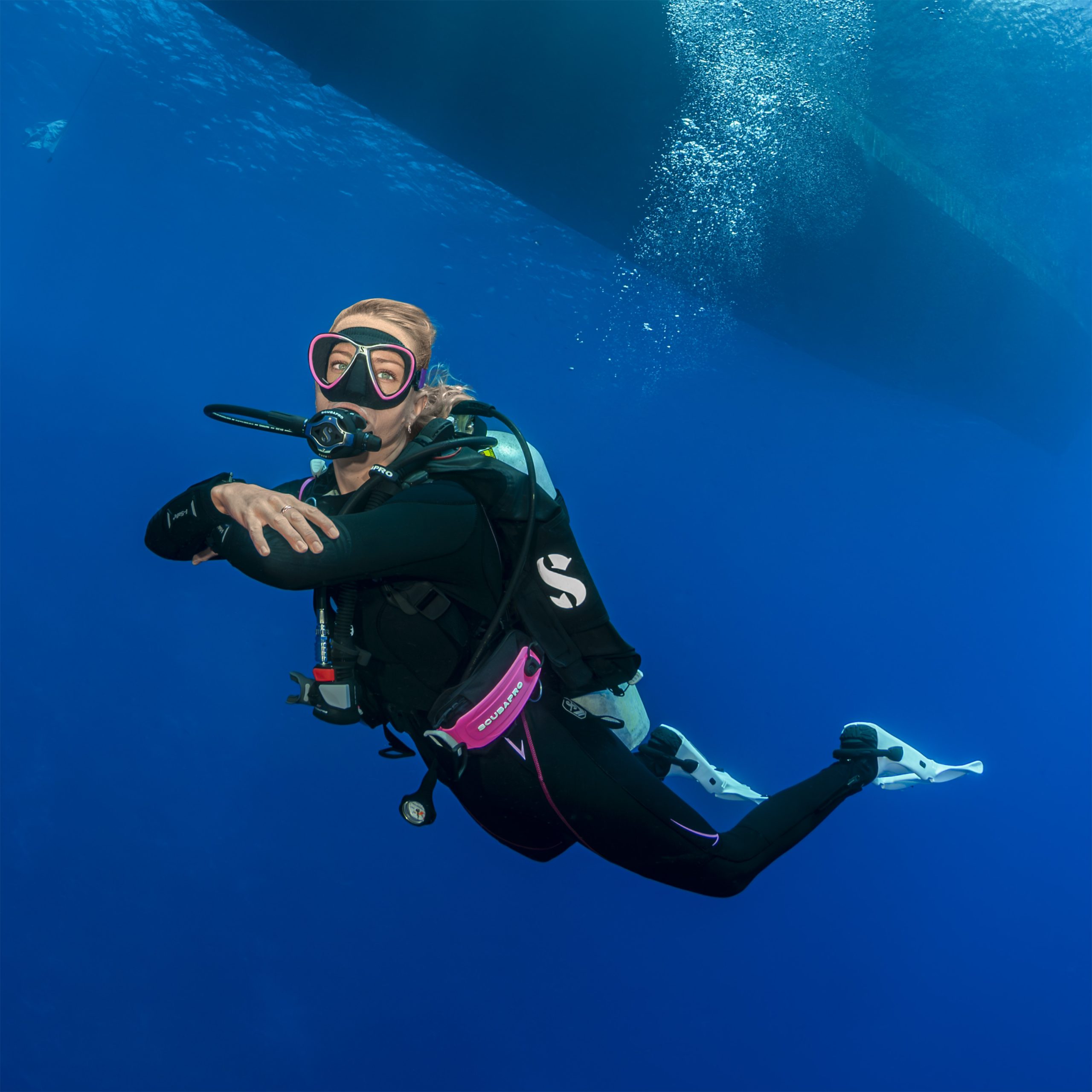 Scuba diver underwater near a large marine vessel.